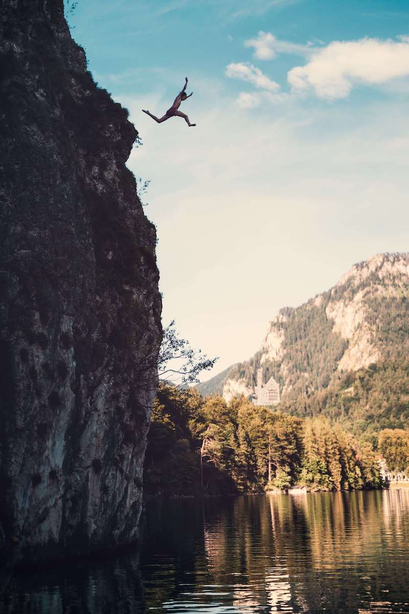 man jumping off a cliff into a lake